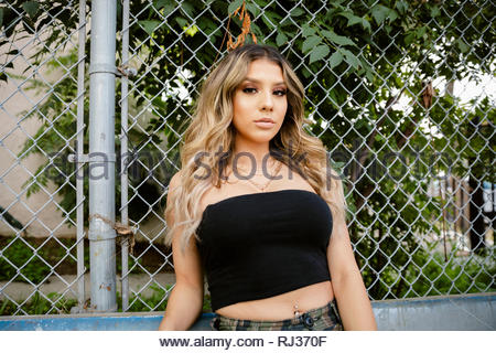 Portrait confident Latinx young woman leaning against fence