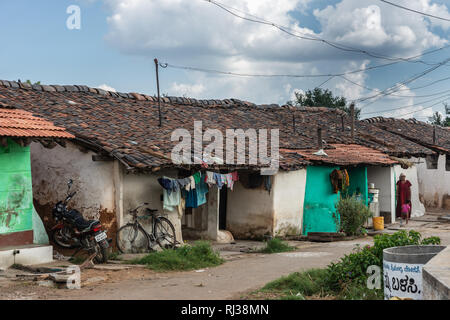 Belavadi, Karnataka, India - November 2, 2013: Closeup of row of small dwellings with mother and child under blue sky with white clouds. Colorful laun Stock Photo