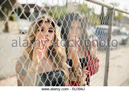 Portrait confident, tough Latinx young women friends behind fence