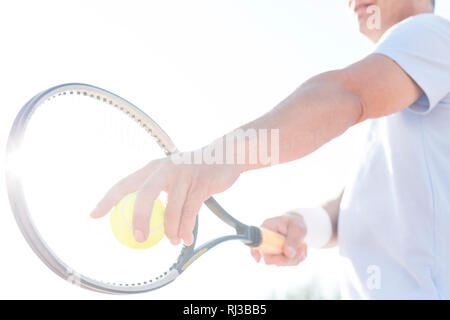 Midsection of mature man serving tennis ball against clear sky on sunny day Stock Photo