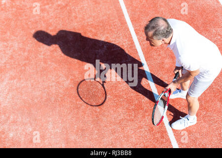 Full length of senior man playing tennis on red court during summer weekend Stock Photo