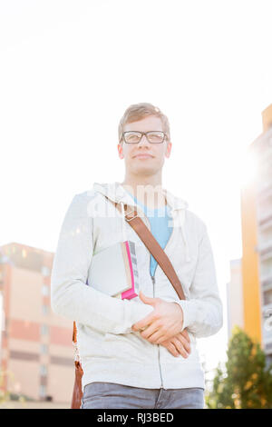 Portrait of handsome student with books in university campus against sky Stock Photo