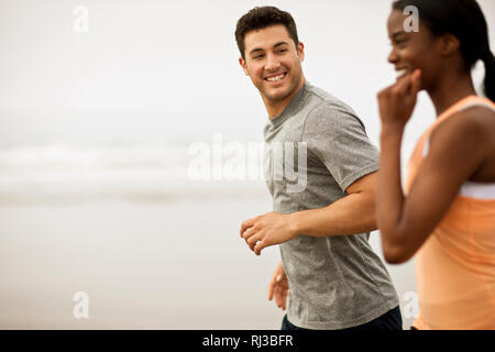 Smiling young couple jogging together on a beach. Stock Photo