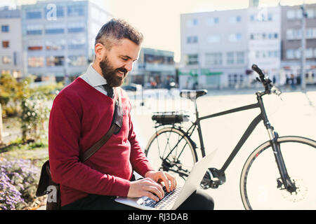 Hipster businessman commuter with bicycle on the way to work in city, using laptop. Stock Photo
