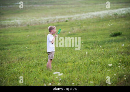 A small boy in nature on a summer day, blowing soap bubbles. Stock Photo