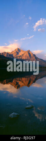 USA, Idaho, Sawtooth National Recreation Area, Sawtooth National Forest, Sunrise on McGown Peak, with moon over the mountain, is reflected in Stanley  Stock Photo