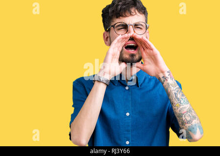 Young handsome man wearing glasses over isolated background Shouting angry out loud with hands over mouth Stock Photo