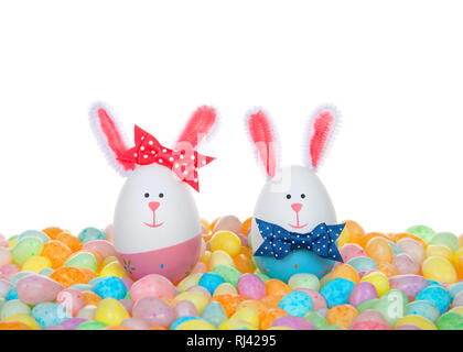 Easter Eggs crafted into bunnies, boy and girl, wearing bow tie and bow on ear sitting in a colorful pile of speckled jelly beans. Stock Photo