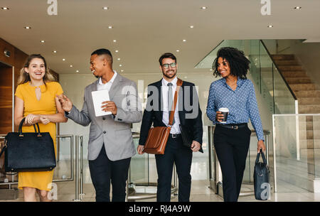 Two young business professionals standing together and discussing over business report in office hallway. Office colleagues reviewing a business docum Stock Photo