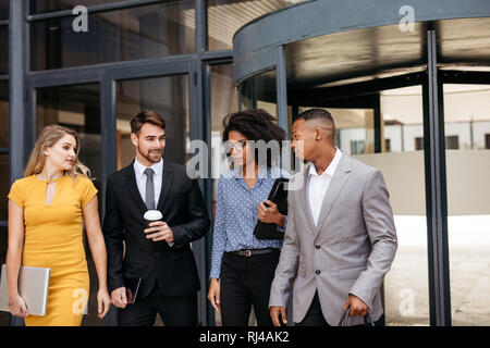 Group of corporate professionals walking out of office together and talking. business men and women walking through office hallway. Stock Photo