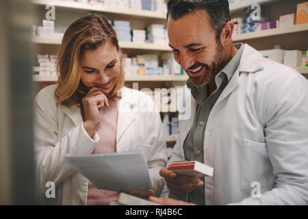 Two dedicated male and female pharmacists looking for the best medicine in the stock while working together in a pharmacy. Pharmacists holding prescri Stock Photo