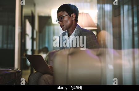 Mature african woman at hotel lobby using laptop. Female on business trip using laptop in hotel lobby. Stock Photo