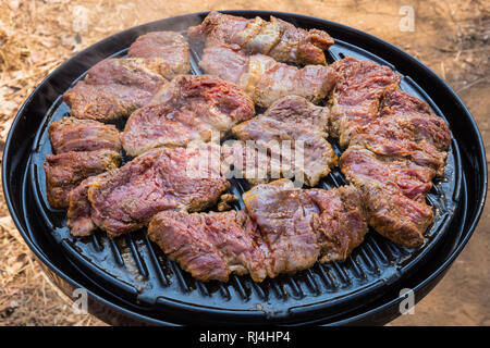 Pieces of steak cooking on a round BBQ (barbecue) outdoors. Stock Photo