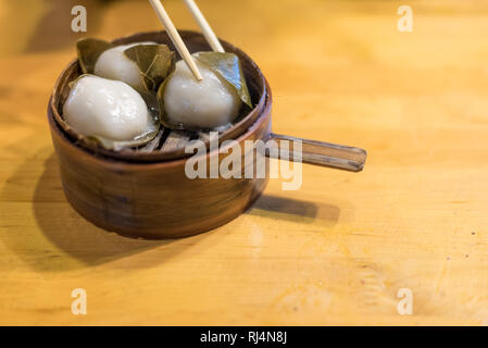 Glutinous rice dumplings wrapped in fresh leaves on a wooden table Stock Photo
