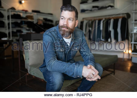 Confident male business owner sitting in menswear clothing shop