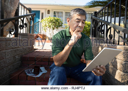 Latinx senior man using digital tablet on front stoop