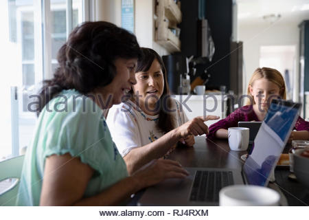 Latinx daughter teaching senior mother how to use laptop at kitchen table