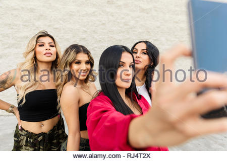 Tough young Latinx women taking selfie with camera phone