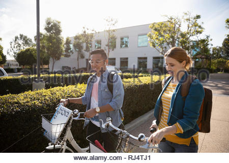 business people walking bicycles in sunny parking lot