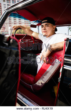 Portrait confident, cool Latinx young man in low rider vintage car