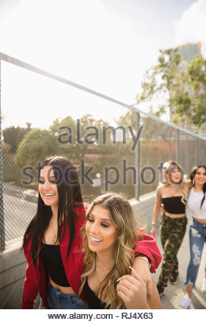 Happy Latinx young women friends walking along urban overpass fence