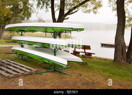 After season kayaks drying on stand on shore in Autumn, water sport equipment waiting for tourists in morning autumn fog, Poland, nobody, Stock Photo