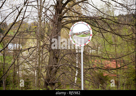 Convex roadside traffic mirror sign post installed in risk area with limited visibility, road reflection traffic safety in Poland, Europe, Trees behin Stock Photo