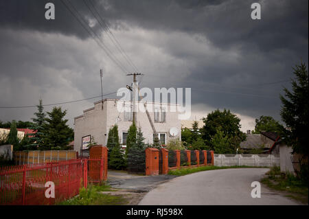 Gloomy stormy weather above brick house with antenna on roof in Odrzywol, Poland, Europe, Building, red bricks gate and fence, fir with spruce trees a Stock Photo