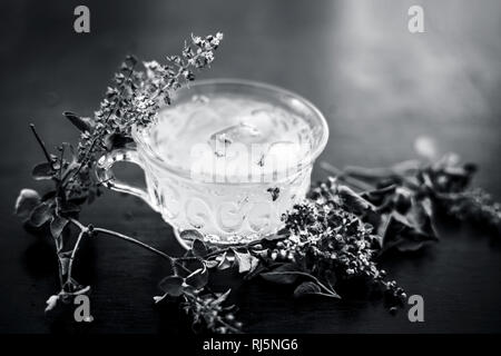 White colored Ice tea in a transparent cup on brown colored wooden surface with some ice cubes and fresh bright leaves of holy basil. Stock Photo