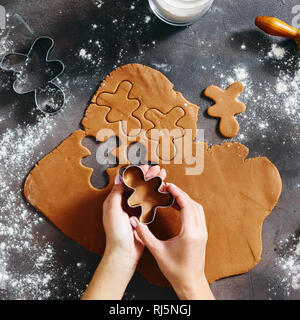 Flat lay christmas food concept. Woman is cooking gingerbread man cookies in Christmas on dark background, top view. Xmas dessert Stock Photo