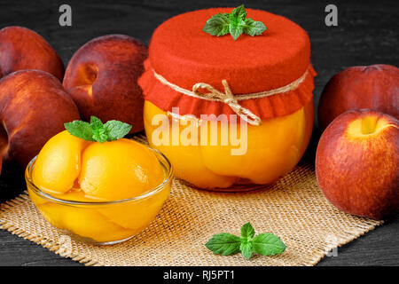 Peach compote with half peaches in glass jars on an old black wooden table(selective focus). Stock Photo