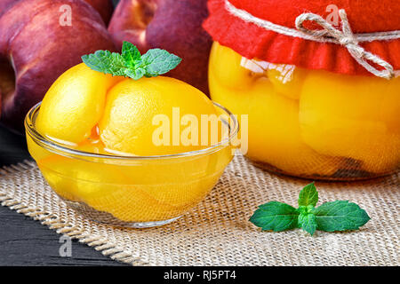 Peach compote with half peaches in glass jars on an old black wooden table(selective focus). Stock Photo