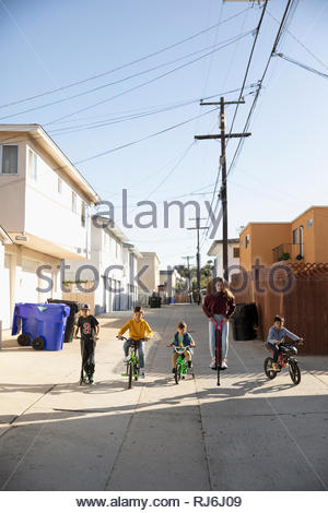 Latinx children playing, riding bikes and scooter in sunny alley