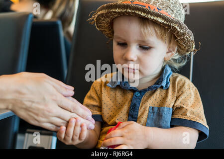 A portrait of a young 2 year old boy holding his mothers hand. Stock Photo