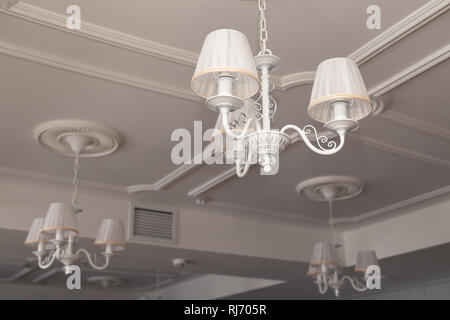 Chandeliers with three electric lamps and lampshades hanging on ceiling. Concept cozy evening in the hotel, theater during intermission Stock Photo