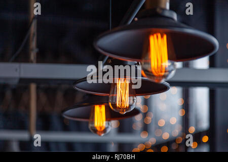 Black iron loft chandeliers with edison lamps on a black background, bokeh. Concept of modern interior design of a restaurant, cafe, apartment, office Stock Photo