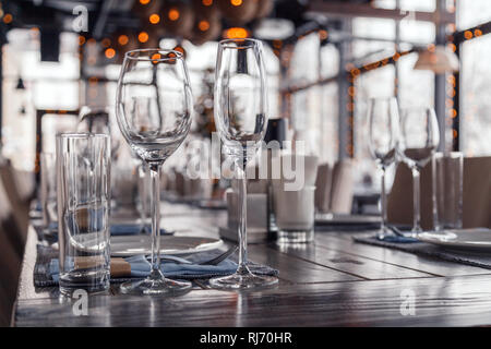 Restaurant interior, serving, wine and water glasses, plates, forks and knives on textile napkins stand in row on vintage gray wooden table. Concept b Stock Photo