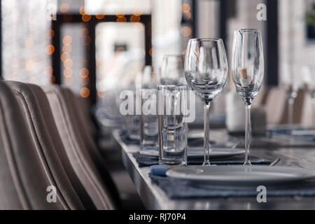 Restaurant interior, serving, wine and water glasses, plates, forks and knives on textile napkins stand in row on vintage gray wooden table. Concept b Stock Photo