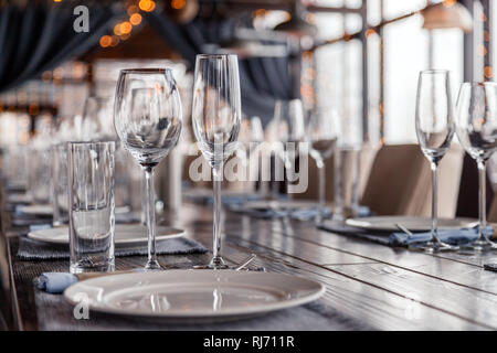 Restaurant interior, serving, wine and water glasses, plates, forks and knives on textile napkins stand in row on vintage gray wooden table. Concept b Stock Photo