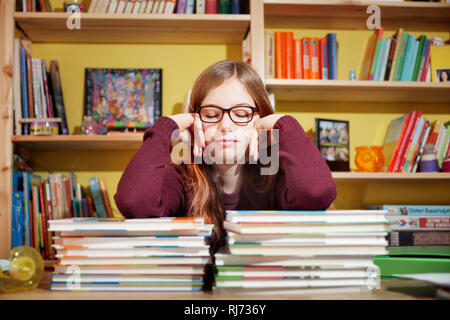 Mädchen, 10 Jahre alt, ermüdet von den Hausaufgaben, vor einem Stapel Bücher, mit geschlossenen Augen Stock Photo