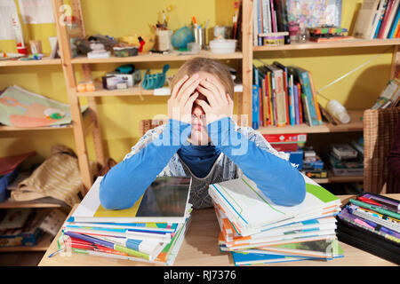 Mädchen, 10 Jahre alt, bei den Hausaufgaben, vor einem Stapel Bücher, überfordert Stock Photo