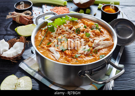 hearty spicy Mulligatawny soup with chicken meat sprinkled with fried cashew in a metal pot on a black wooden table with ingredients,  Indian and engl Stock Photo
