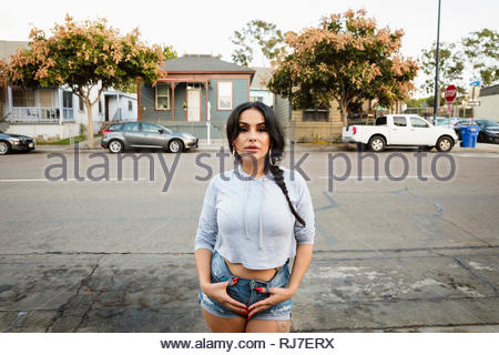 Portrait confident, tough Latinx young woman on neighborhood street