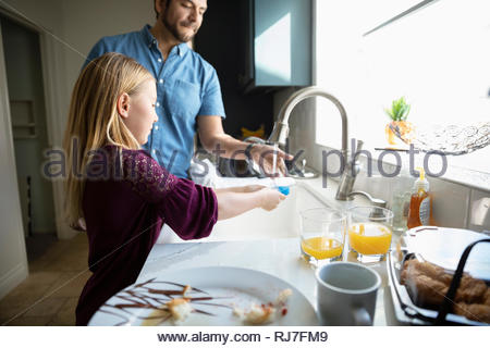 Latinx father and daughter doing dishes at kitchen sink