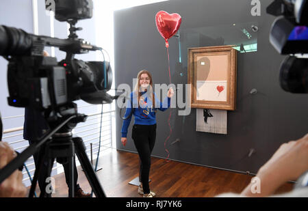 Baden Baden, Germany. 05th Feb, 2019. Oleksandra Parkhanova, a visitor of the Frieder Burda Museum, stands with a red heart balloon at the shredded Banksy picture 'Love is in the Bin'. The work will be shown there from 05.02.2019 to 03.03.2019. Originally it was called 'Girl with Balloon'. Since it destroyed itself during an art auction in London, it has been called 'Love is in the Bin'. Banksy later presented the action as an attack on the art market. Credit: Uli Deck/dpa/Alamy Live News Stock Photo
