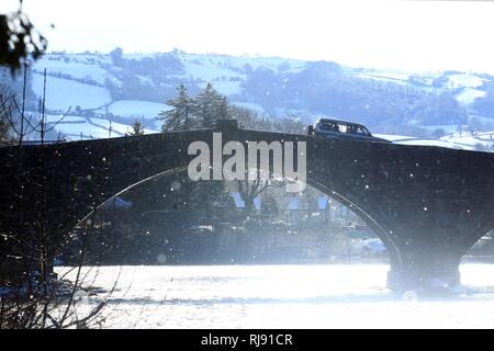 A car crosses Pont Fawr in Llanrwst with snow covered hills in the background. Thursday 8th March 2018. Stock Photo