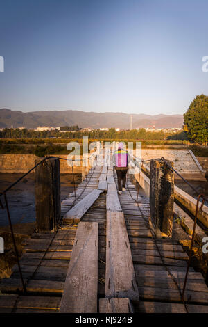 Woman with basket on her back crossing footbridge near Shaxi historic market town, Yunnan, China Stock Photo