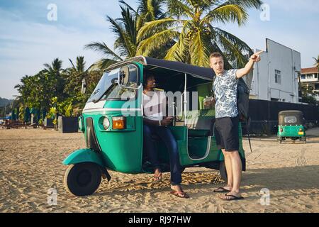 Tuk tuk driver with passenger against sand beach in Sri Lanka. Stock Photo