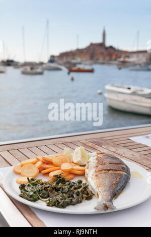Teller mit Fisch, Kartoffeln und Spinat in einem Restaurant am Hafen Rovinj, Istrien, Kroatien Stock Photo