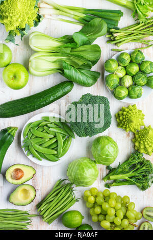 Healthy eating vegan concept. Green vegetables fruits on white table broccoli sprouts peas avocado courgette beans bok choy celery apple grapes, top v Stock Photo